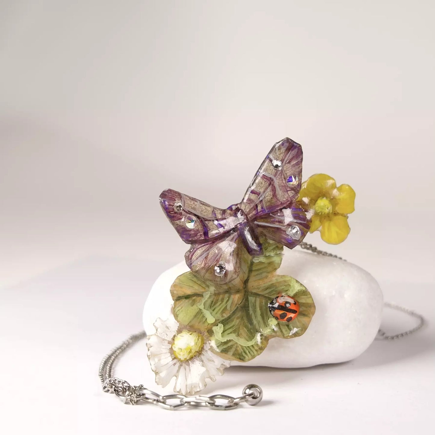 Gioiello artigianale in resina con fiori, farfalla e vero quadrifoglio